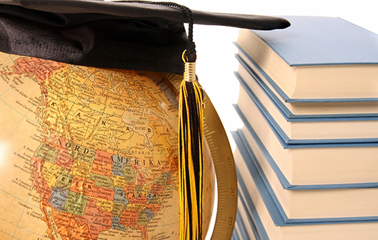 Globe with black mortarboard on top with stack of books next to it